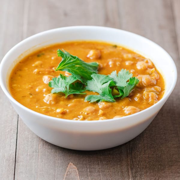 A white bowl of New York Grill's halal chickpea stew, garnished with fresh cilantro, on a wooden table.
