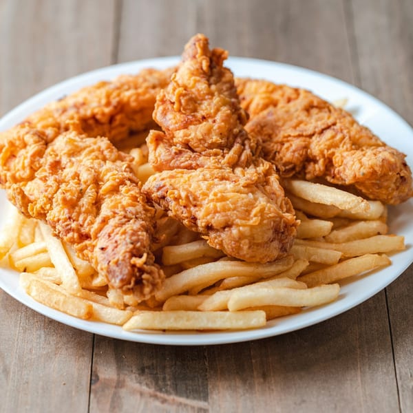 A white plate filled with golden-brown fried chicken tenders and crispy french fries on a wooden table.