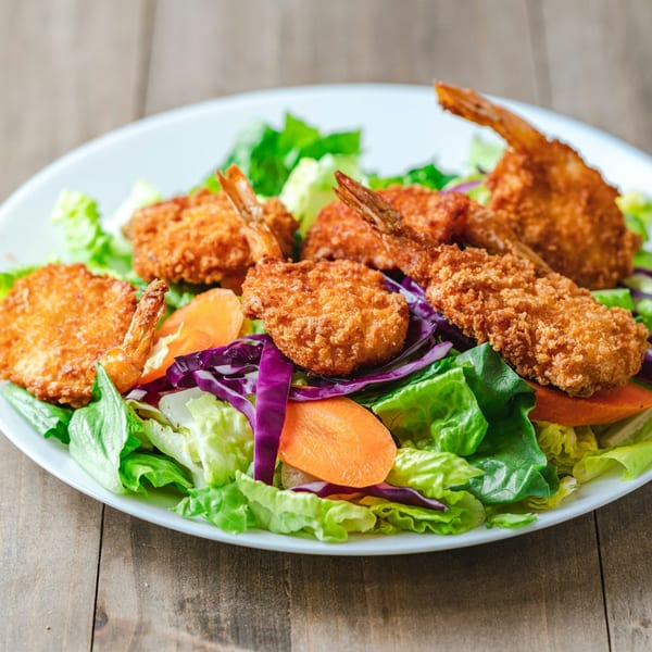Crispy fried shrimp and fresh mixed greens salad with carrots and red cabbage on a white plate.