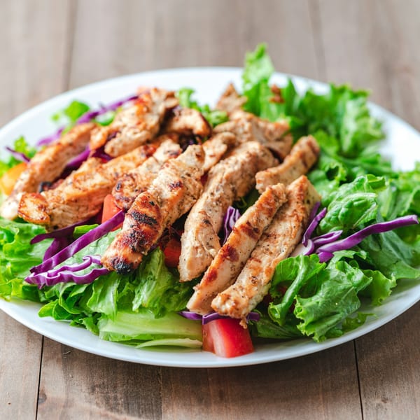 Grilled chicken strips on a bed of fresh green lettuce, red cabbage, and diced tomatoes.